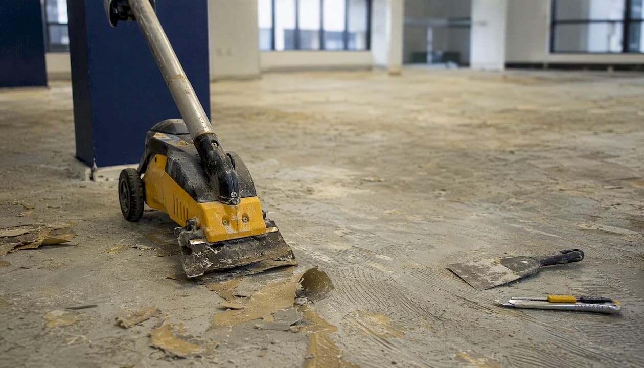 Floor scraper and tools on adhesive-covered office floor