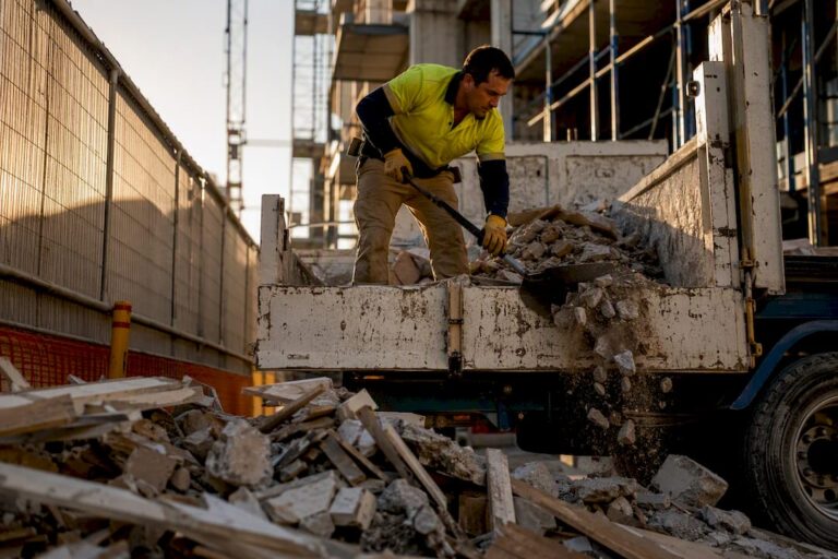 Worker loading construction rubble into rubbish truck